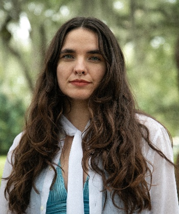 Woman with long brown hair, wearing white and aqua looking forward